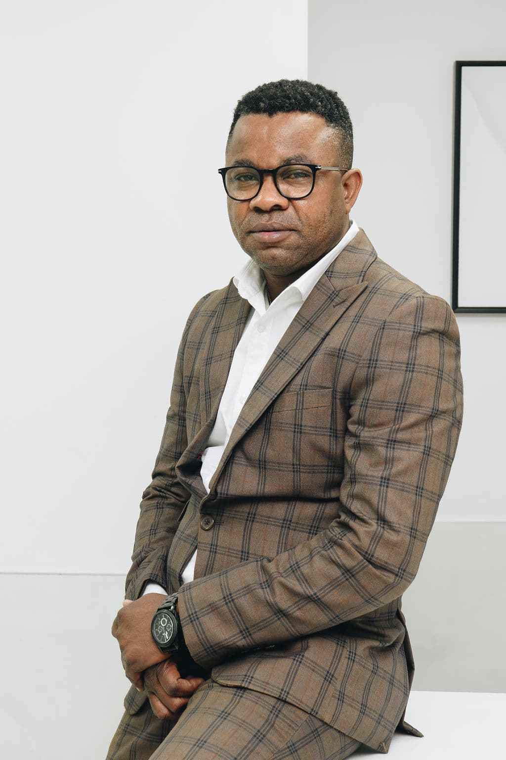 Portrait of Dr Malonda Makanda in a brown check suit and white shirt, seated against a plain white wall